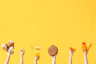 Birçok el farklı plaj aksesuarları ve sarı arka planda kokteyl tutuyor.