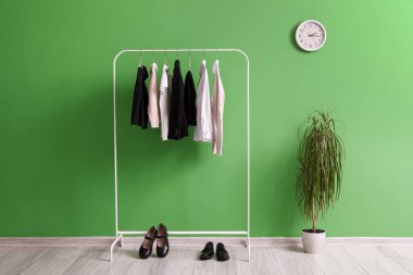 Süslü okul üniforması, ayakkabılar, ev bitkisi ve saat ile dolu raflar yeşil duvarda asılı.