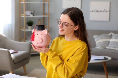 Mezuniyet şapkalı domuz kumbarası tutan mutlu kız öğrenci. Öğrenci kredisi kavramı