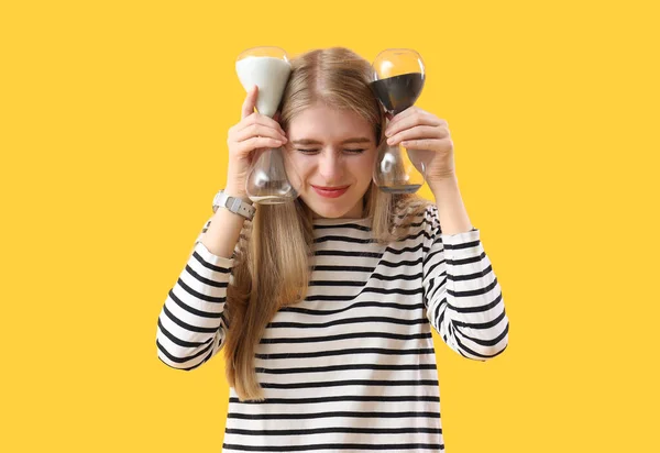 Stressed young woman with hourglass on yellow background. Deadline concept