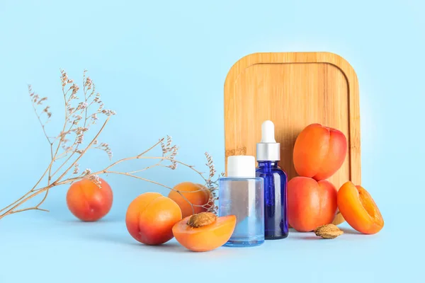 Composition with bottles of cosmetic products, ripe apricots and wooden board on color background