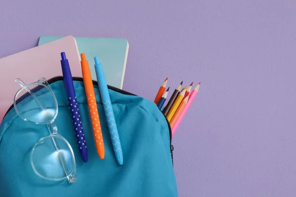 Blauer Schulrucksack Mit Verschiedenen Papeterie Und Brille Auf Lila Hintergrund — Stockfoto