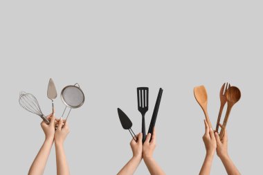 Gri arka planda farklı pişirme aletleri olan kadın elleri