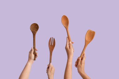 Leylak arka planında ahşap pişirme aletleri olan kadın eller.