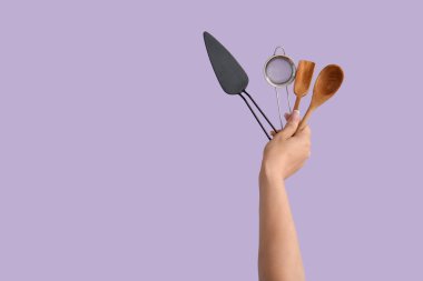 Leylak arka planında pişirme aletleri olan kadın eller.