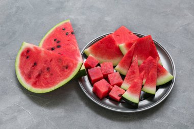Gri zemin üzerinde taze karpuz parçaları olan bir tabak.