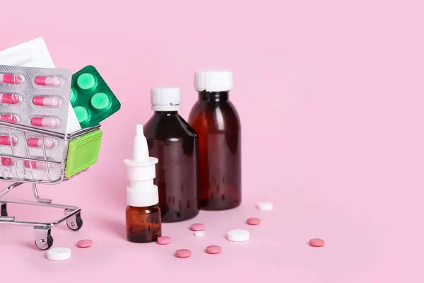 Mini shopping cart with different medicines on pink background