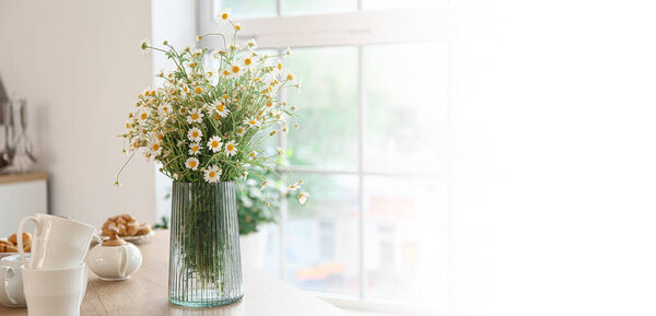 Vase with fresh chamomiles on table in kitchen. Banner for design