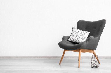 Beyaz duvarın yanında şık gri koltuk, yastık ve fener.