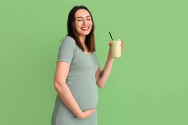 Yeşil arka planda bir bardak smoothie ile genç hamile kadın