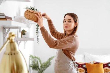 Yatak odasında toz beziyle rafı temizleyen genç bir kadın.