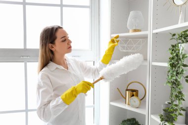 Genç bir kadın evinde toz beziyle rafı temizliyor.