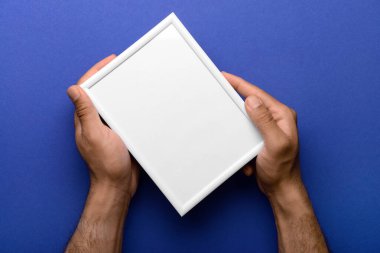 Mavi arkaplanda boş fotoğraf çerçevesi tutan adam