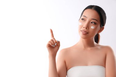 Yüzünde krem olan güzel Asyalı kadın beyaz arka plandaki bir şeyi işaret ediyor.