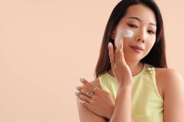 Yüzünde bej rengi krem olan güzel bir Asyalı kadın.
