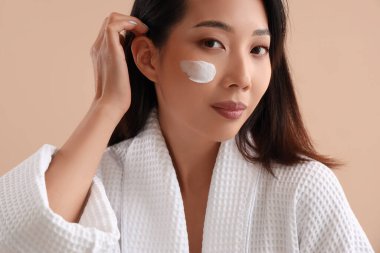 Yüzünde bej rengi krem olan güzel bir Asyalı kadın.