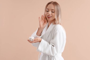 Bej arka planda yüz kremi olan güzel genç bir kadın.