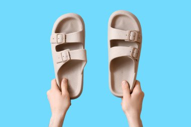 Mavi arka planda yaz sandaletleri olan erkek eller.