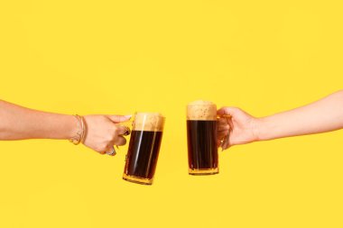 Sarı arka planda soğuk bira kupaları olan kadın elleri.