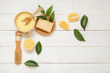 Beyaz ahşap arka planda masaj fırçası ve sabunla bir kase limonlu vücut fırçası.