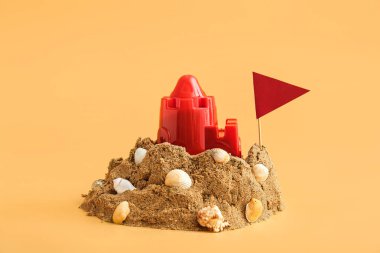 Plaj oyuncağı, deniz kabuğu ve turuncu arka planda bayrak ile kumdan kale