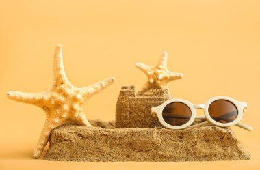 Turuncu arka planda deniz yıldızı ve güneş gözlükleriyle kumdan kale