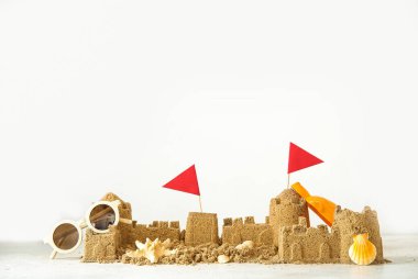 Plaj oyuncağı, güneş gözlüğü ve beyaz arka planda bayraklarla kumdan kale