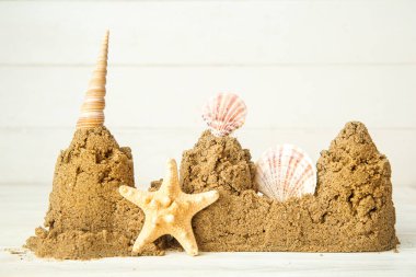 Beyaz ahşap arka planda deniz yıldızı ve deniz kabuklarından yapılmış bir kale.