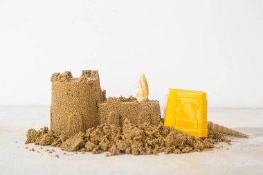 Kumsaldaki oyuncakla kumdan kale ve beyaz arka planda deniz kabuğu.