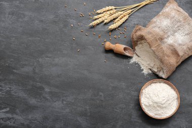 Siyah grunge arka planında buğday unuyla çuval ve kase.