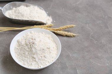 Gri masa üzerinde buğday unu ve çivili kase, yakın plan.