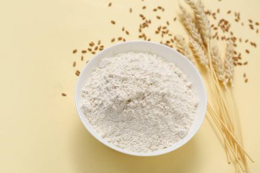 Sarı arka planda buğday unu ve çivili kase.