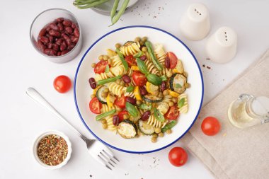 Bir kase domatesli makarna salatası ve beyaz arka planda fesleğen.