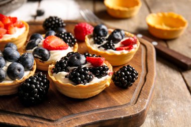 Çırpılmış krema ve ahşap arka planda böğürtlenli lezzetli tartlar.