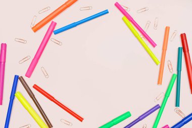 Renkli keçeli kalemlerden ve pembe arkaplandaki ataçlardan yapılmış çerçeve