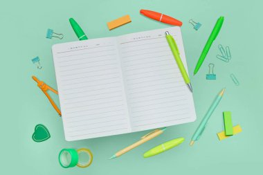 Yeşil zemin üzerinde boş defter ve okul kırtasiyesi olan kompozisyon