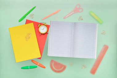 Boş defter, alarm saati ve yeşil arkaplanda okul kırtasiyesi olan kompozisyon