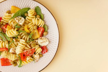 Sarı arka planda biberli ve bezelyeli makarna salatası.