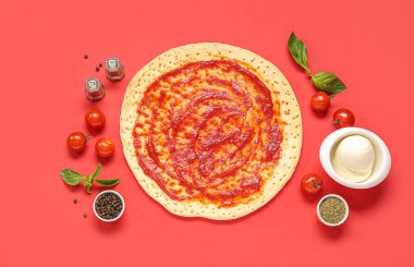 Domates soslu pizza hamuru ve kırmızı arka planda malzemeler.