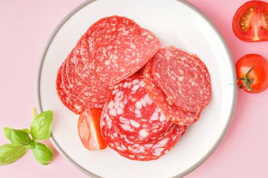 Pembe arka planda lezzetli salam dilimleri olan bir tabak.