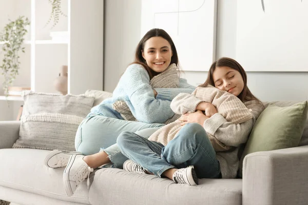 小さな女の子と彼女の母親で暖かいですセーターとともに枕座っていますソファに家 — ストック写真