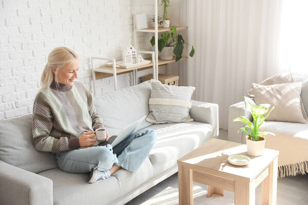 Mature female programmer with cup of coffee and laptop working at home