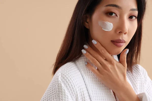 stock image Beautiful Asian woman with cream on her face against beige background