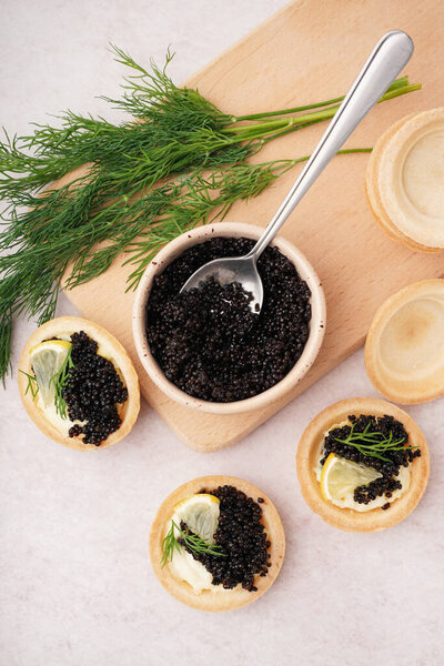 Tasty tartlets with black caviar on light background