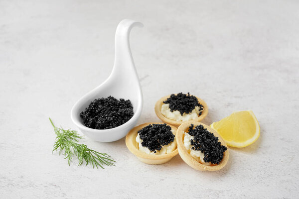 Tasty tartlets with black caviar on light background