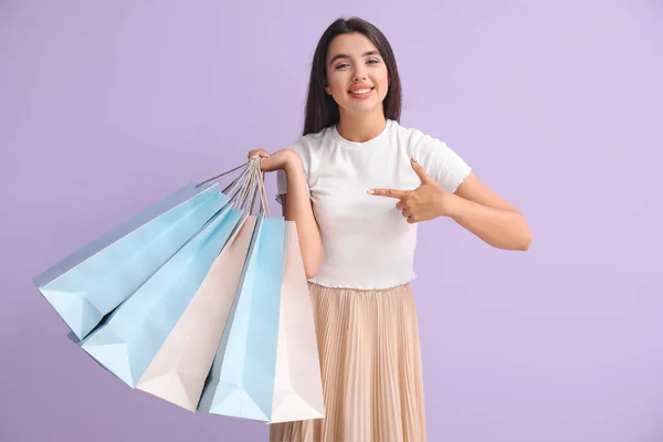 Schöne Junge Frau Zeigt Auf Einkaufstüten Auf Fliederfarbenem Hintergrund — Stockfoto