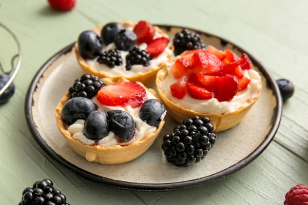 stock image Plate of tasty tartlets with whipped cream and berries on green wooden background