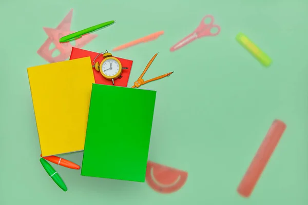 Composition with notebooks, alarm clock and school stationery on green background