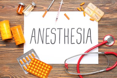 Sözlü anestezi kağıdı ve ahşap arka planda tıbbi malzemeler.