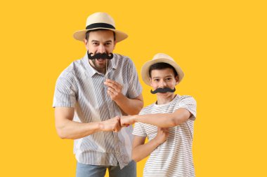 Portrait of father and his little son with paper mustache bumping fists on yellow background clipart